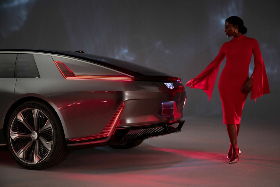 Wide rear three-quarter of the CELESTIQ show car with a woman in red reaching her hand toward the car. Show car images displayed throughout (not for sale).